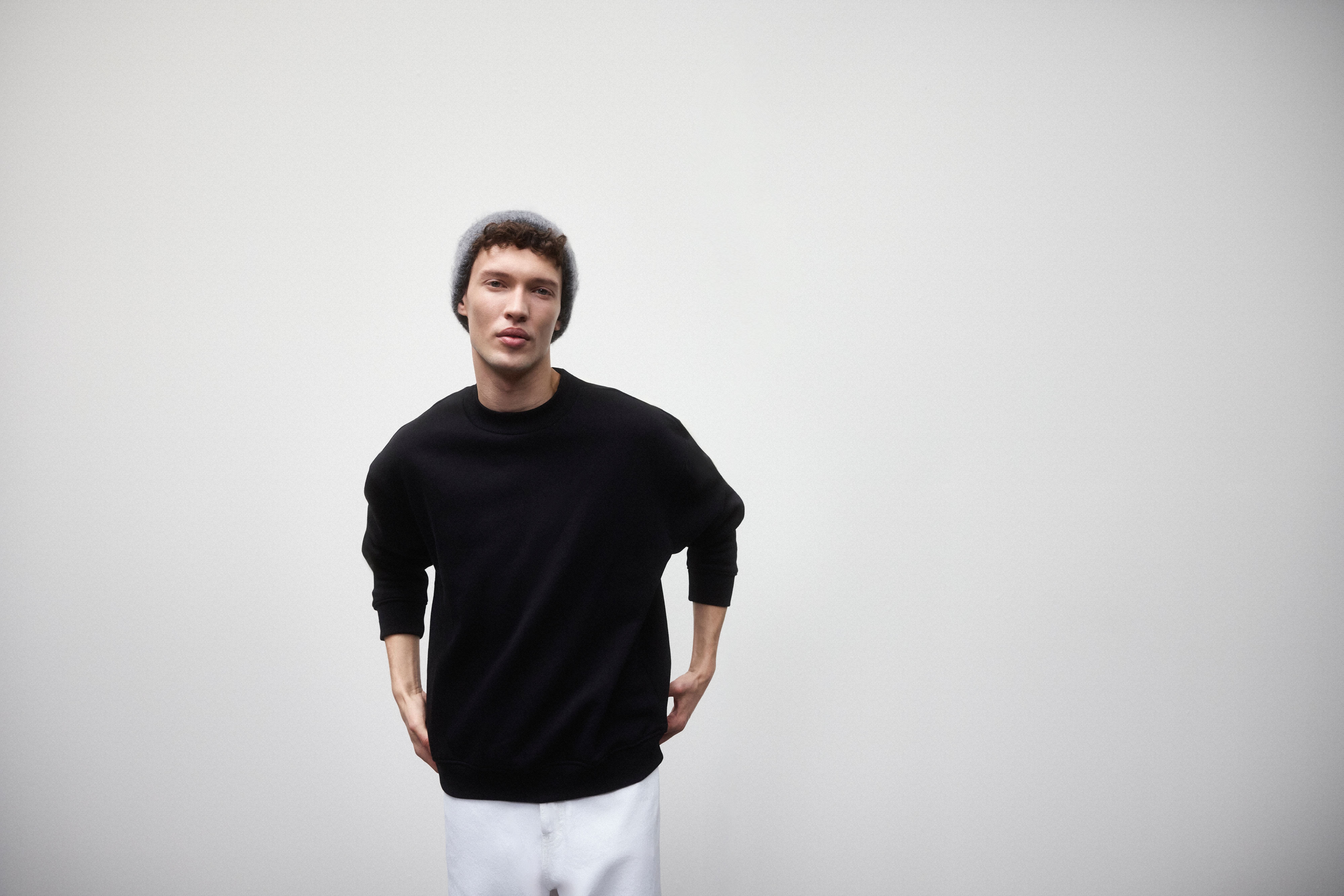 Bărbat purtând un sweatshirt negru, blugi albi și o căciulă gri